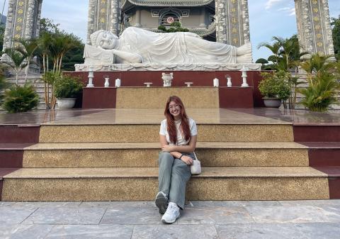 Young woman sitting on some steps in front of a Vietnamese temple