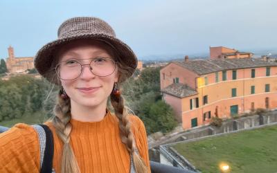 A person with braided hair and glasses is seen upside-down, with a serene waterway and classic Venetian architecture in the background.
