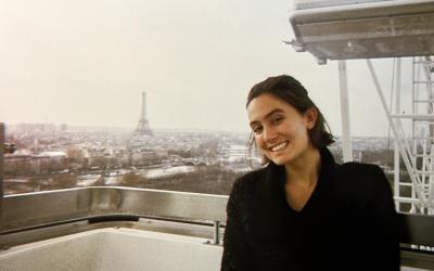 A person smiling, seated on the Ferris wheel with the Eiffel Tower and Paris skyline in the background.